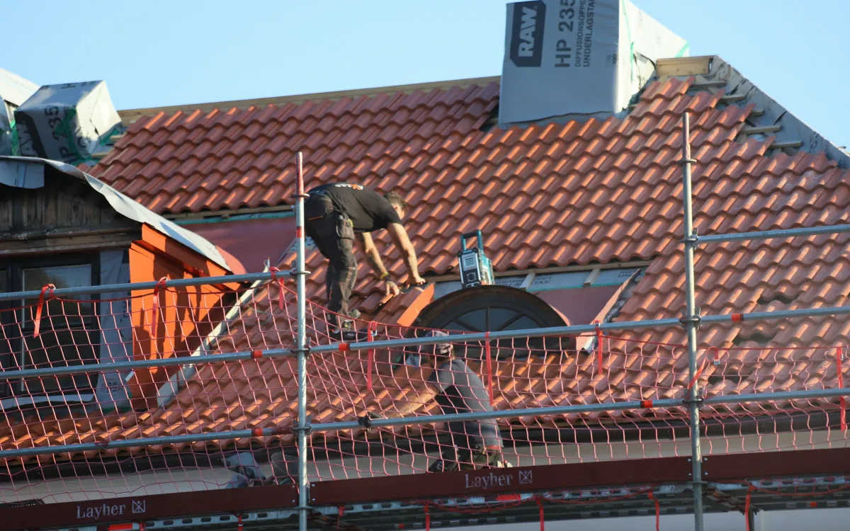 Dachdecker auf dem Gerüst bei der Arbeit an einem roten Ziegeldach