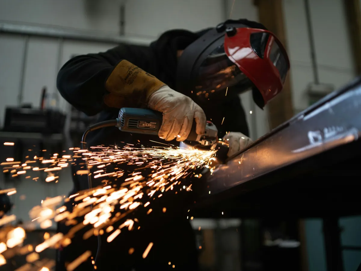 Metallbauer mit Schweißhelm schleift ein Stahlprofil, Funken fliegen